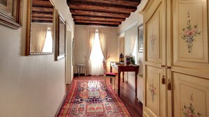 A hallway with a patterned carpet, wooden ceiling beams, and a wooden cabinet with floral designs. - Ca' Riza (Venice)