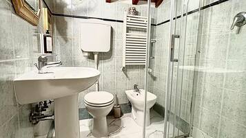 A bathroom with a sink, toilet, bidet, and a glass-enclosed shower.