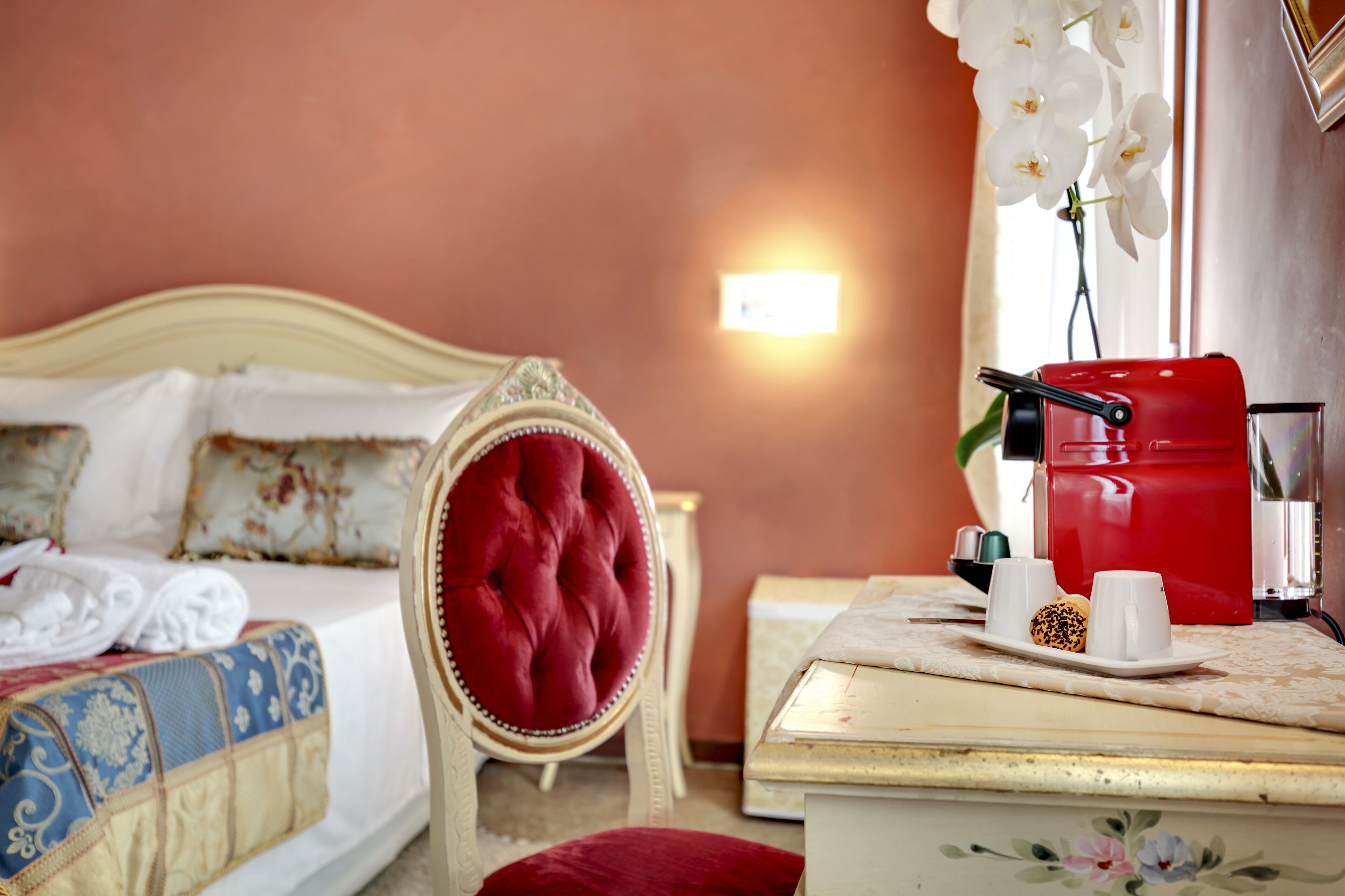 A hotel room with a bed, a red chair, a coffee maker, and a small table with cups and a plate.
