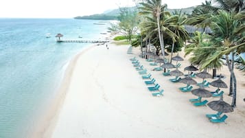 Una playa con agua cristalina, un muelle y filas de sillas azules bajo palmeras.