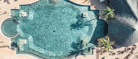 Vista aérea de un área de piscina con una fuente circular, tumbonas y palmeras.