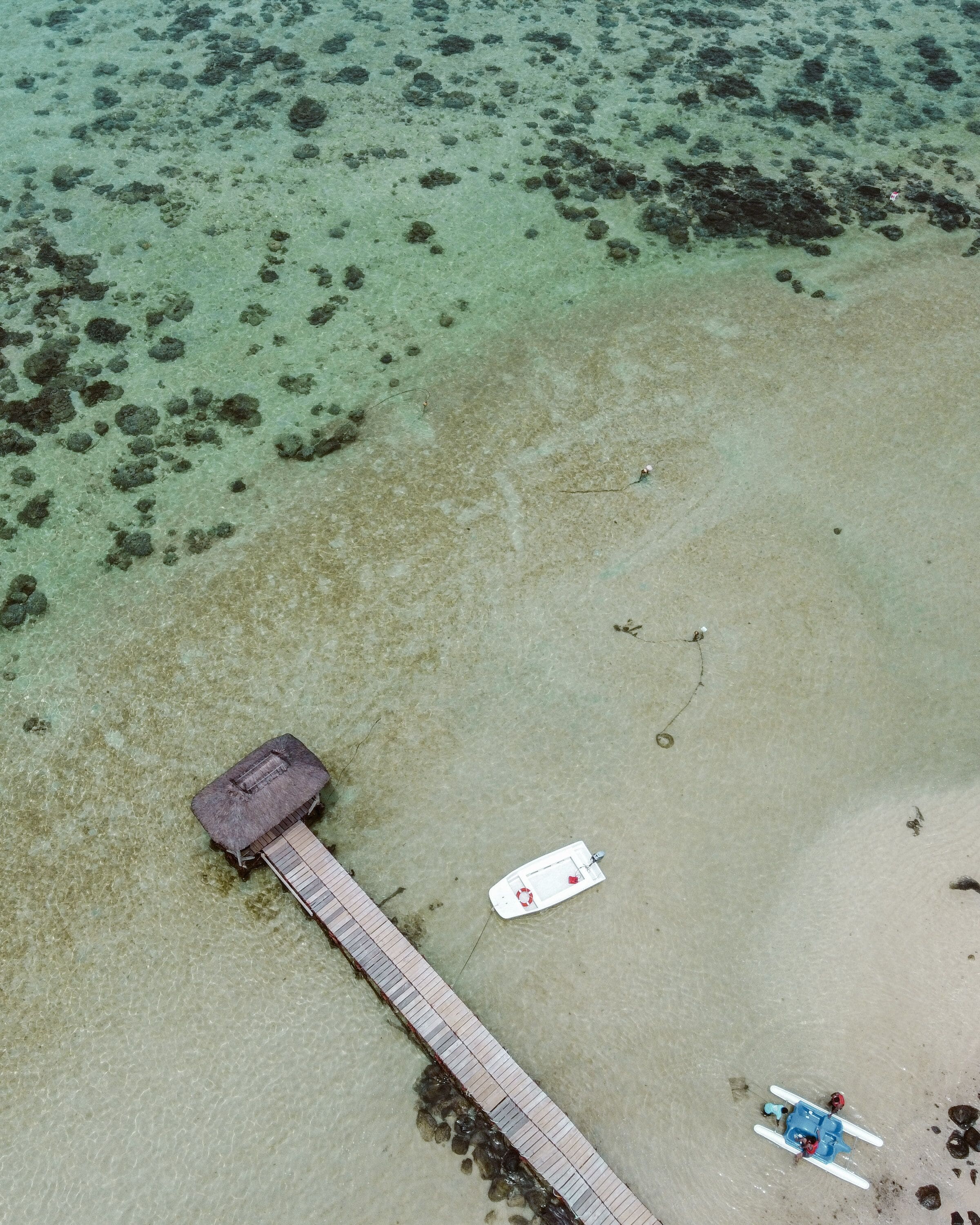 An aerial view of a beach with a pier extending into the water, a small hut, and a boat.