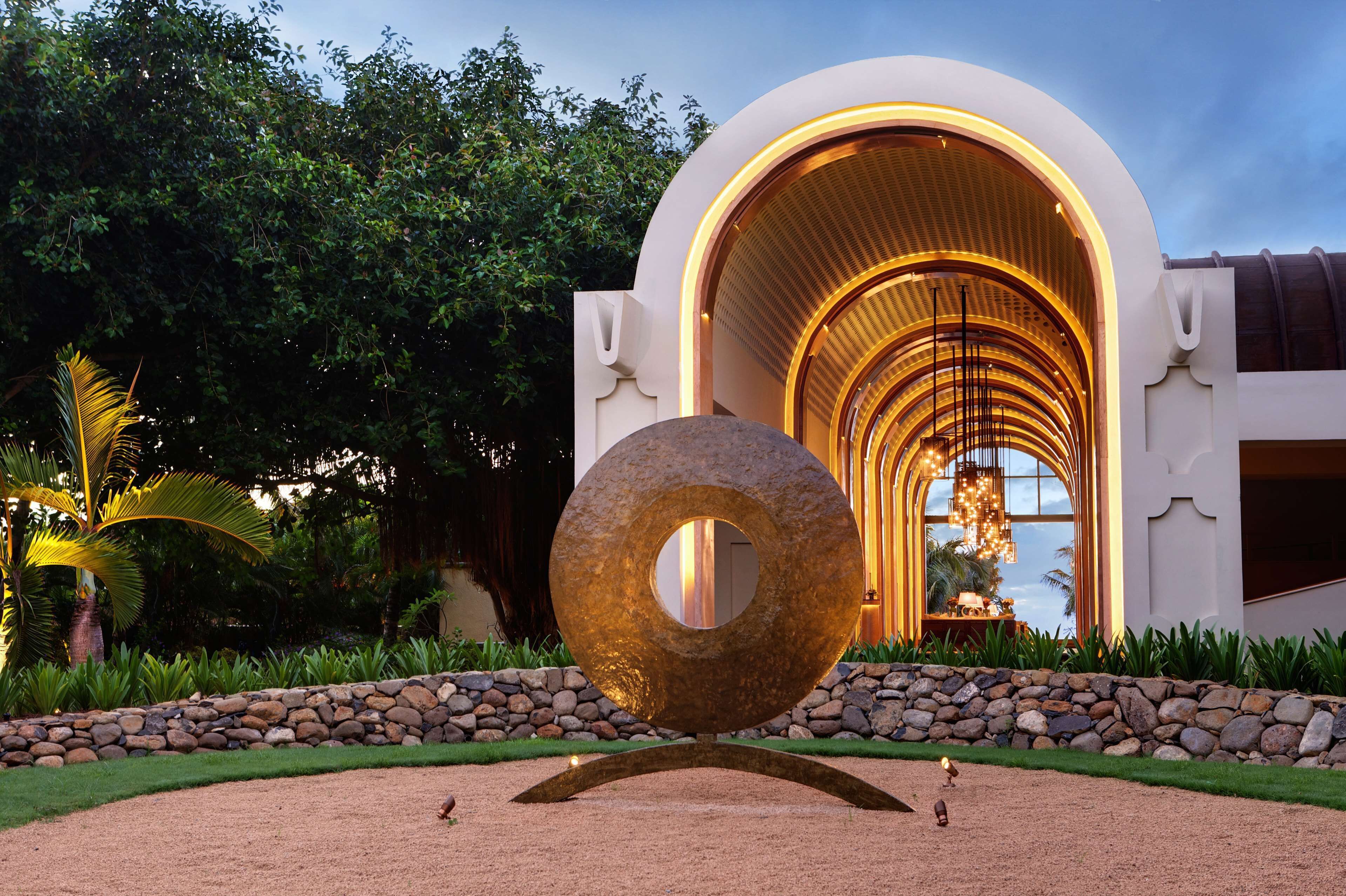 A modern building with a circular sculpture in front, surrounded by a landscaped garden.