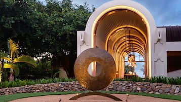 A modern building with a circular sculpture in front, surrounded by a landscaped garden.
