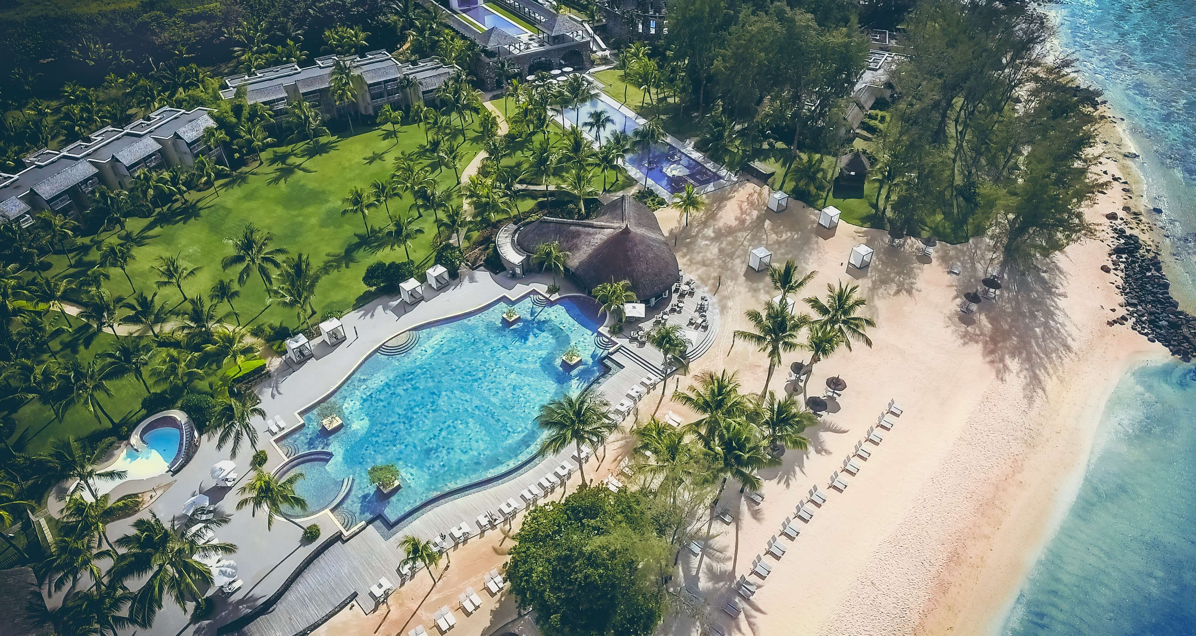 Vista aerea di un resort con piscina, spiaggia e palme.