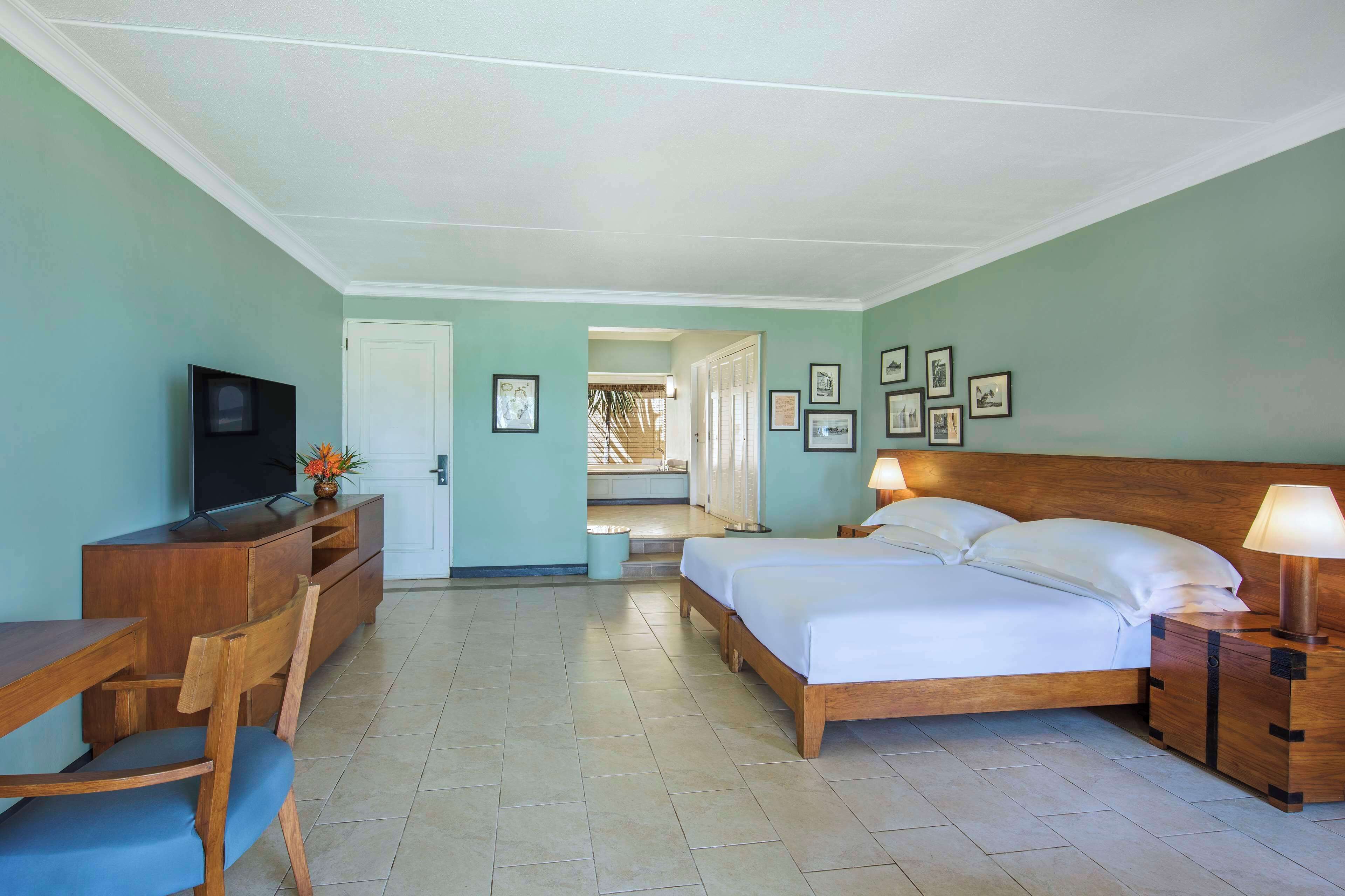 A hotel room with a bed, bedside table, TV, desk, chair, and framed pictures on the wall.
