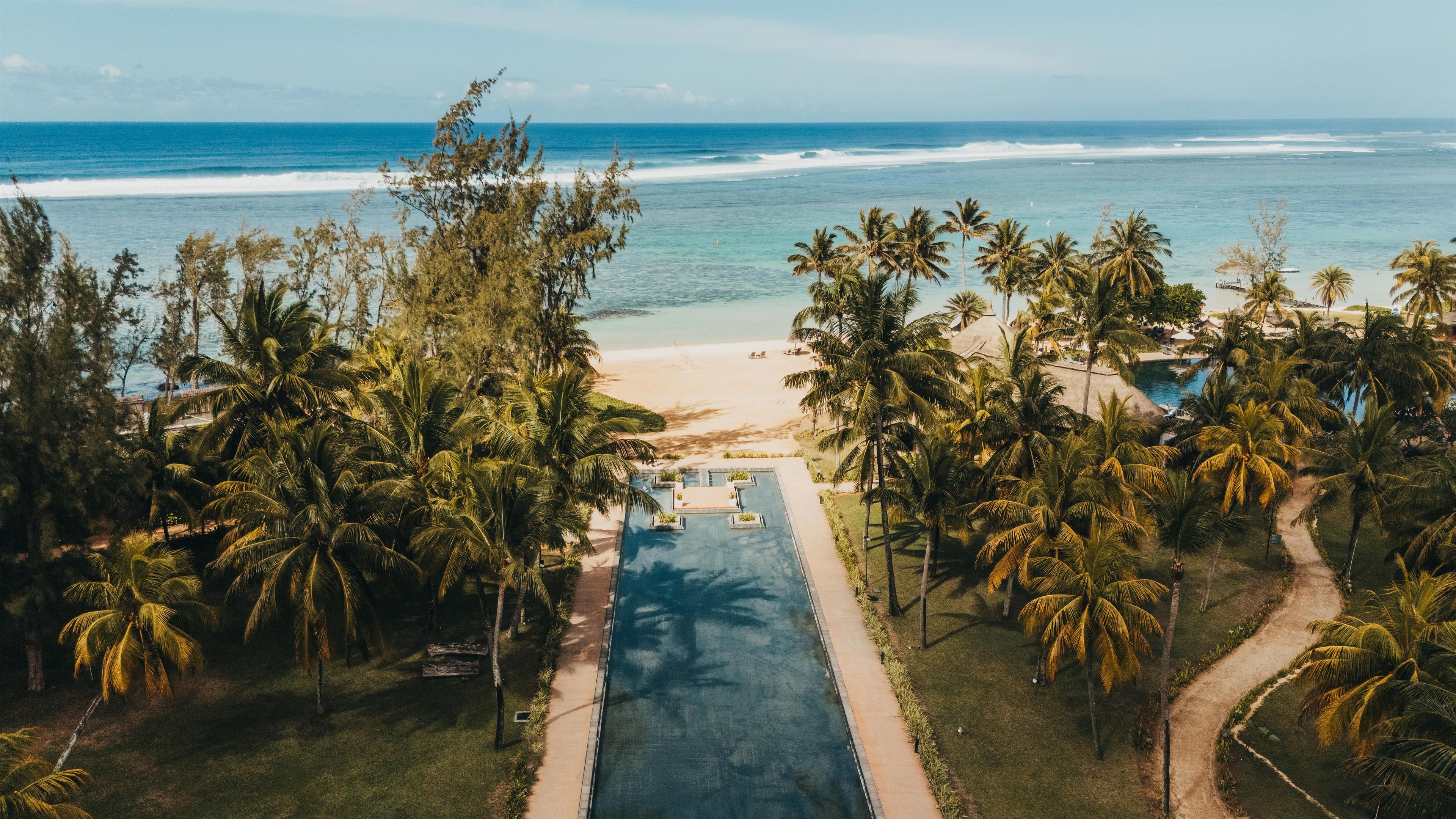 A tropical resort with a swimming pool, palm trees, and a beach.