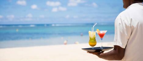 A person holding a tray with two drinks on a beach.