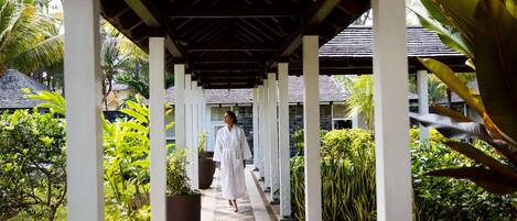 A covered walkway with a person in white, surrounded by lush greenery and potted plants.