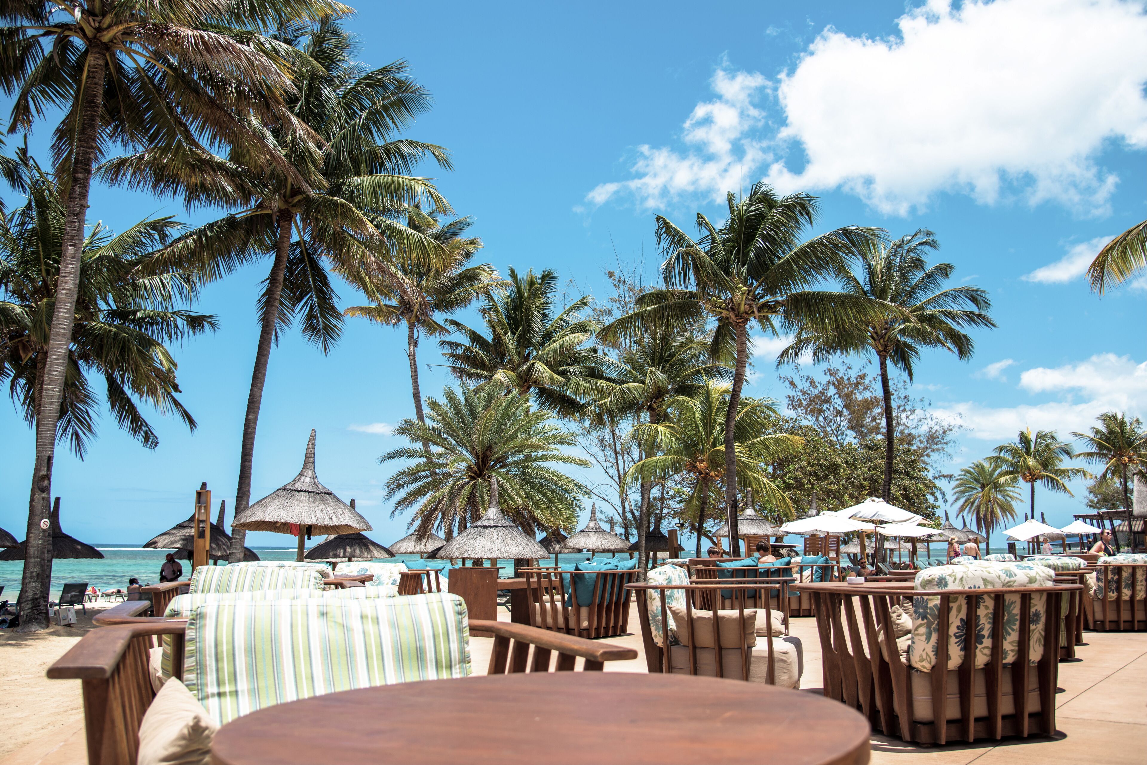 Un ristorante sulla spiaggia con posti a sedere all'aperto, palme e vista sull'oceano.