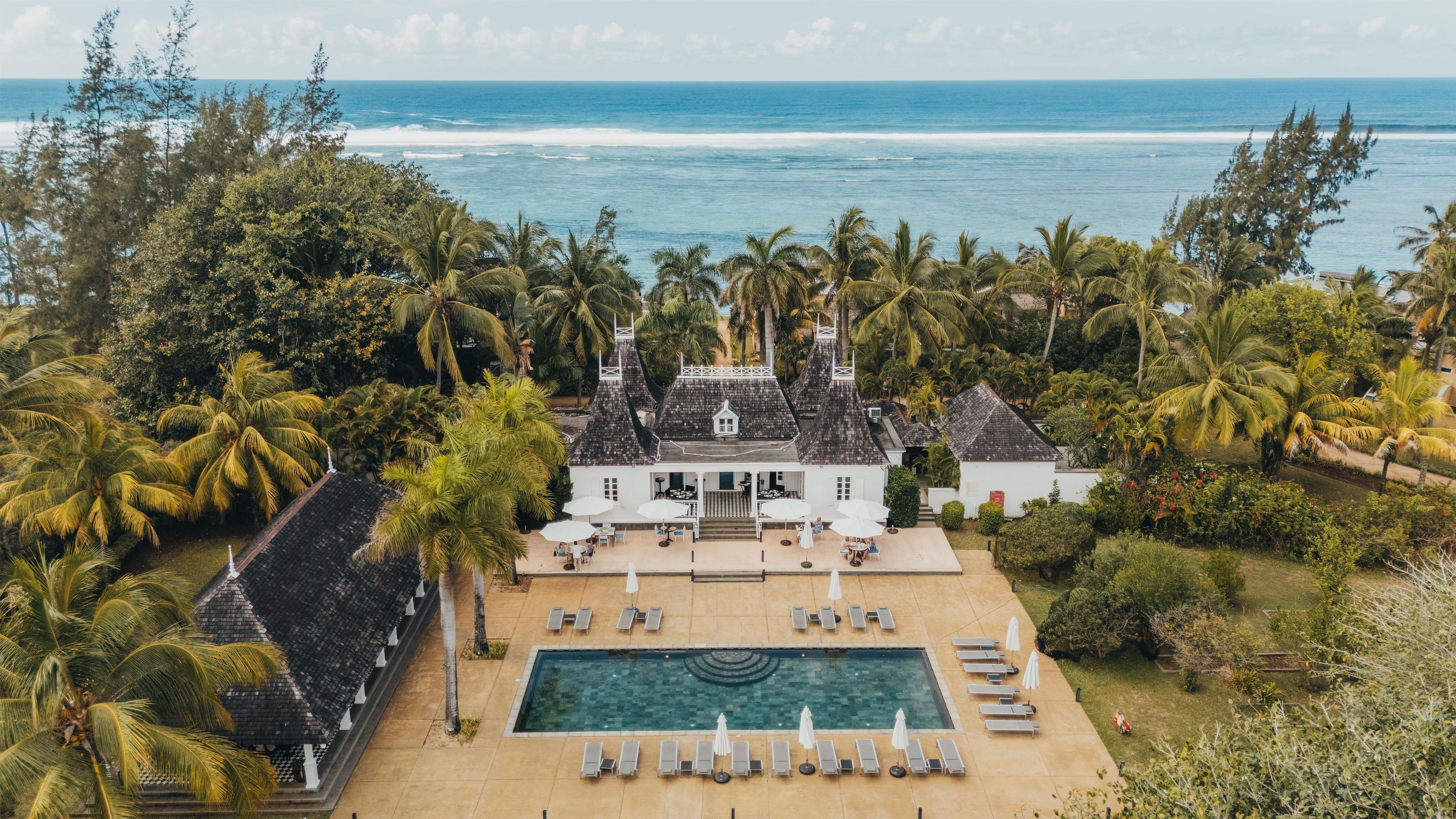 A beachfront property with a swimming pool, lounge chairs, and a view of the ocean.