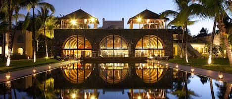 Un hotel con piscina reflectante, ventanas arqueadas y palmeras.