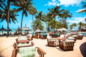 A beachside resort with outdoor seating, palm trees, and a view of the ocean. - OUTRIGGER Mauritius Beach Resort (Bel Ombre)
