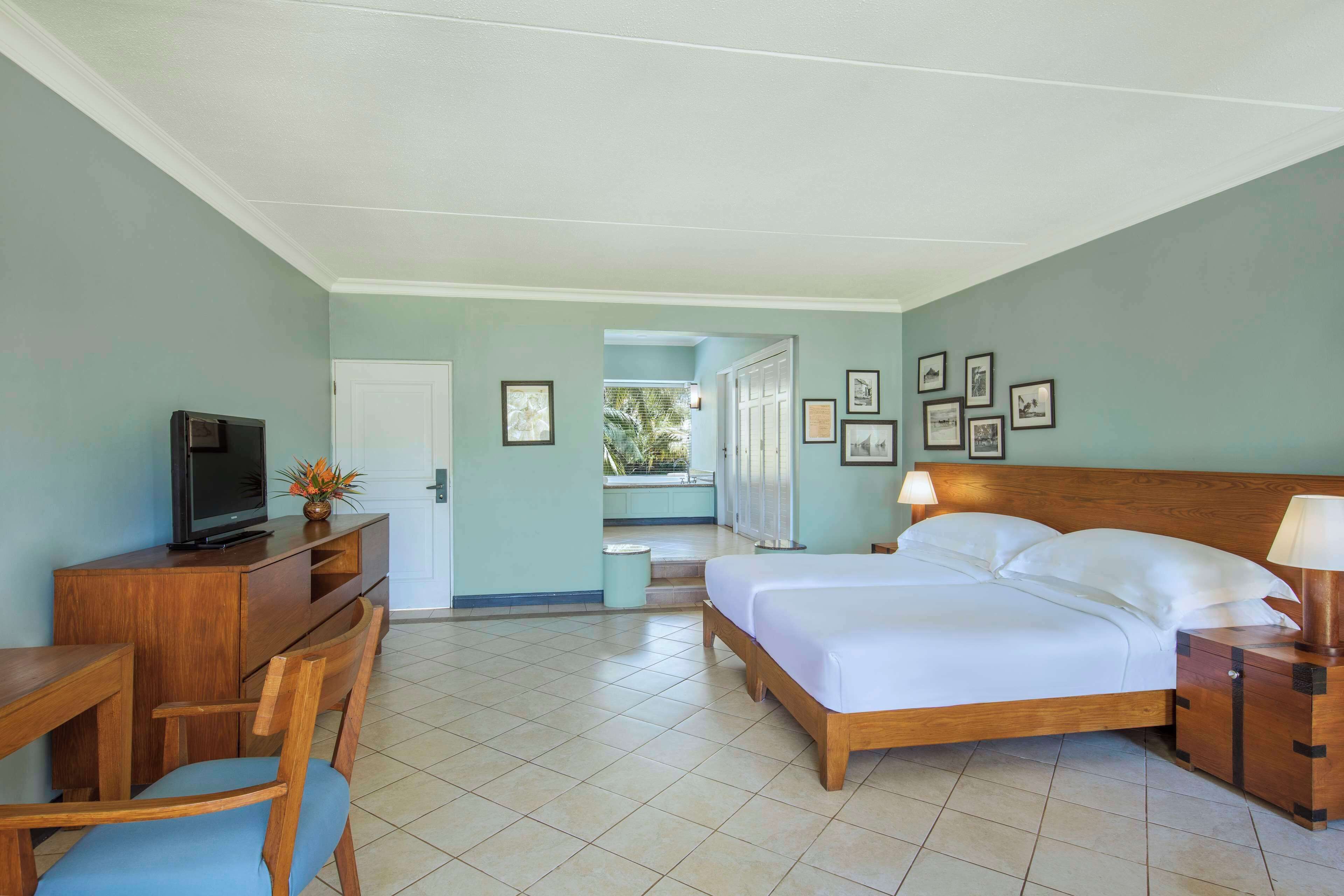 Habitación de hotel con cama, escritorio, silla, televisor y cuadros en la pared.