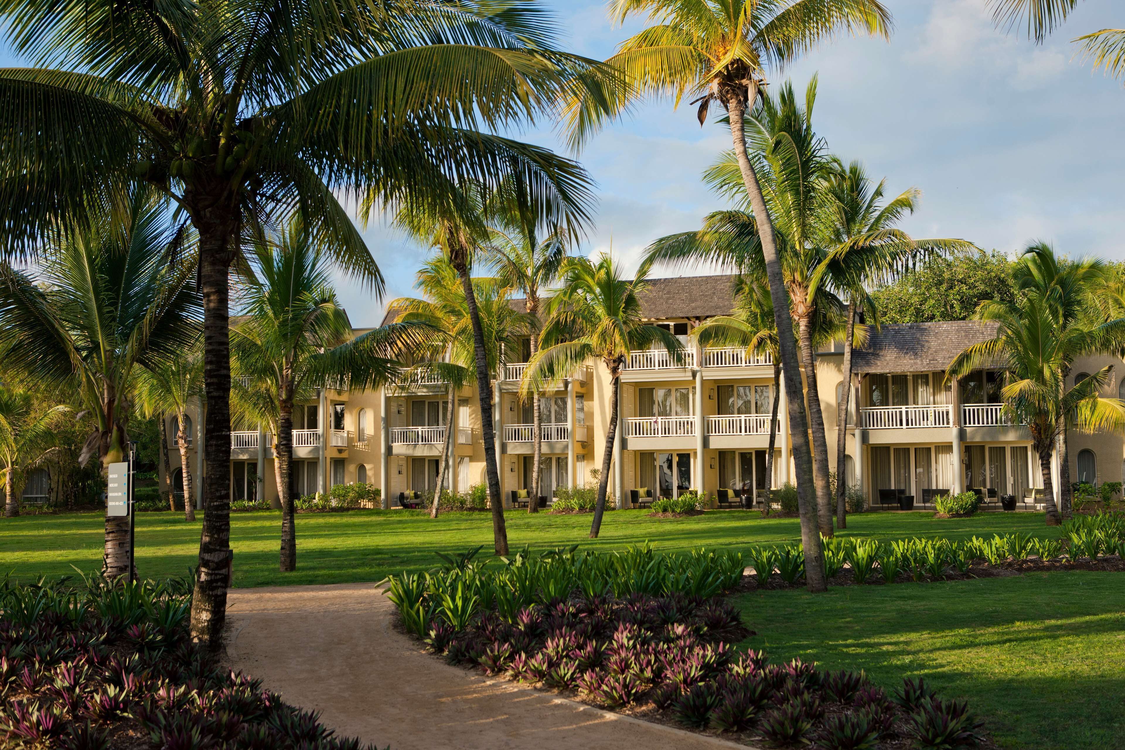 A resort with multiple-story buildings, palm trees, and a well-maintained lawn.