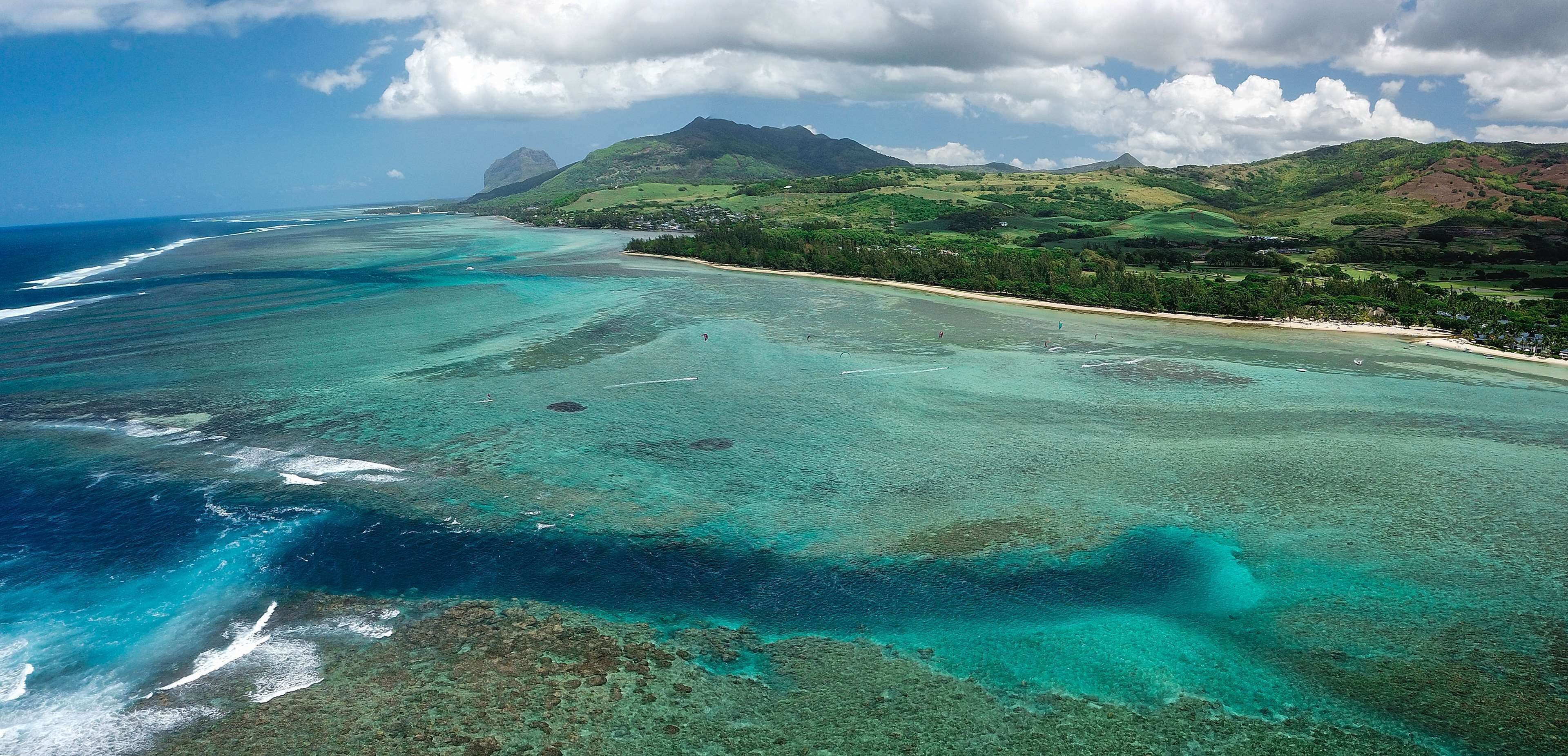 A coastal landscape with clear turquoise waters, a sandy beach, and green hills in the background.