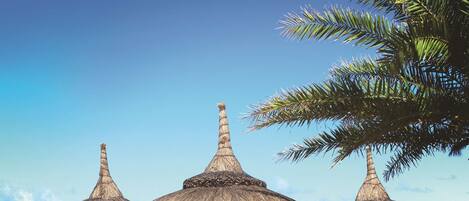 A beach with thatched umbrellas, lounge chairs, and a couple walking.