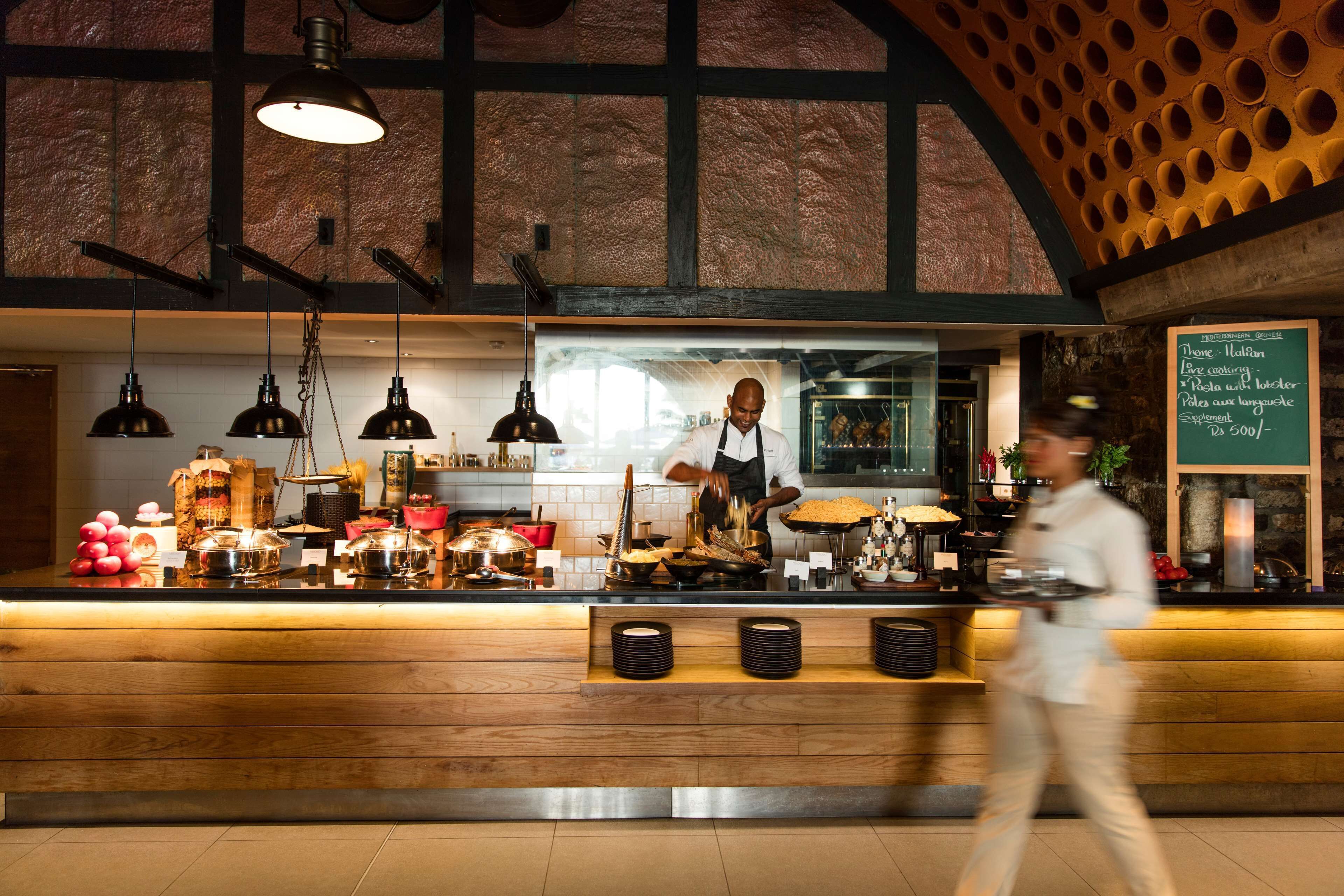 A restaurant counter with a chef preparing food, a menu board, and a modern interior design.