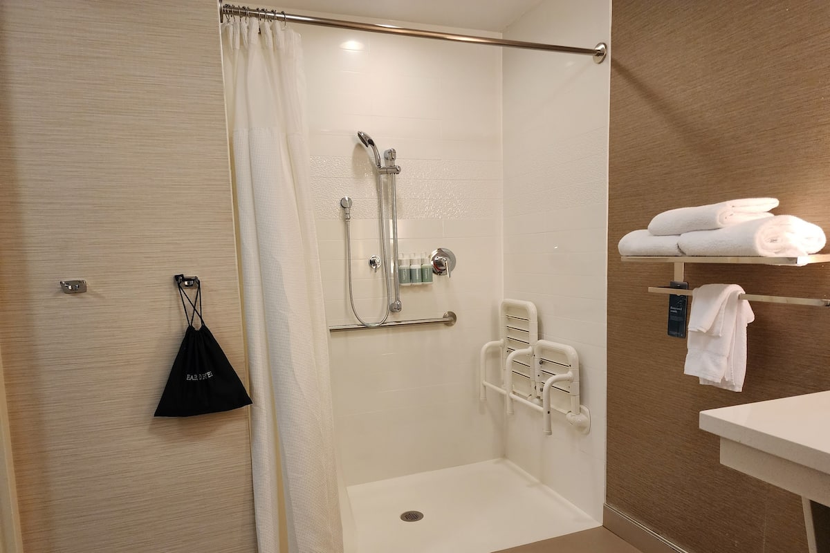 A modern bathroom with a shower, grab bars, a towel rack, and a small sink.