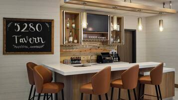 Zona de bar moderna con un letrero de pizarra que dice '5280 Tavern', taburetes, una caja registradora y una variedad de botellas y vasos.