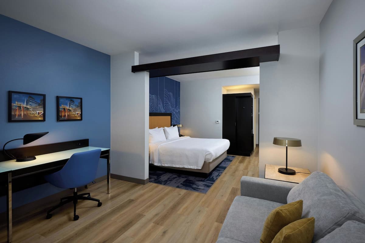 A modern hotel room with a desk, chair, bed, and a sofa.