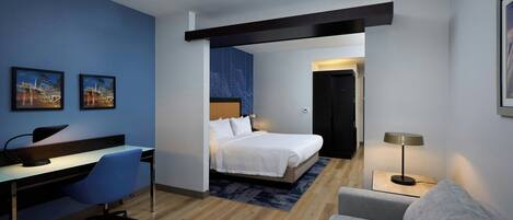 A modern hotel room with a desk, chair, bed, and a sofa.