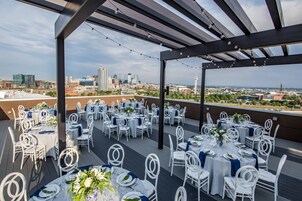 Un espacio al aire libre en la azotea con mesas dispuestas para un evento formal, con vistas a un horizonte urbano.