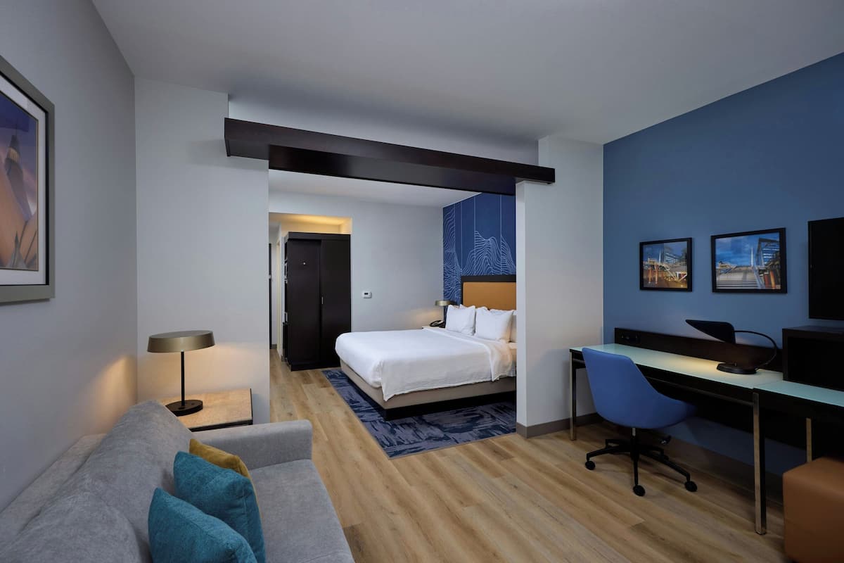 A modern hotel room with a bed, desk, and seating area.