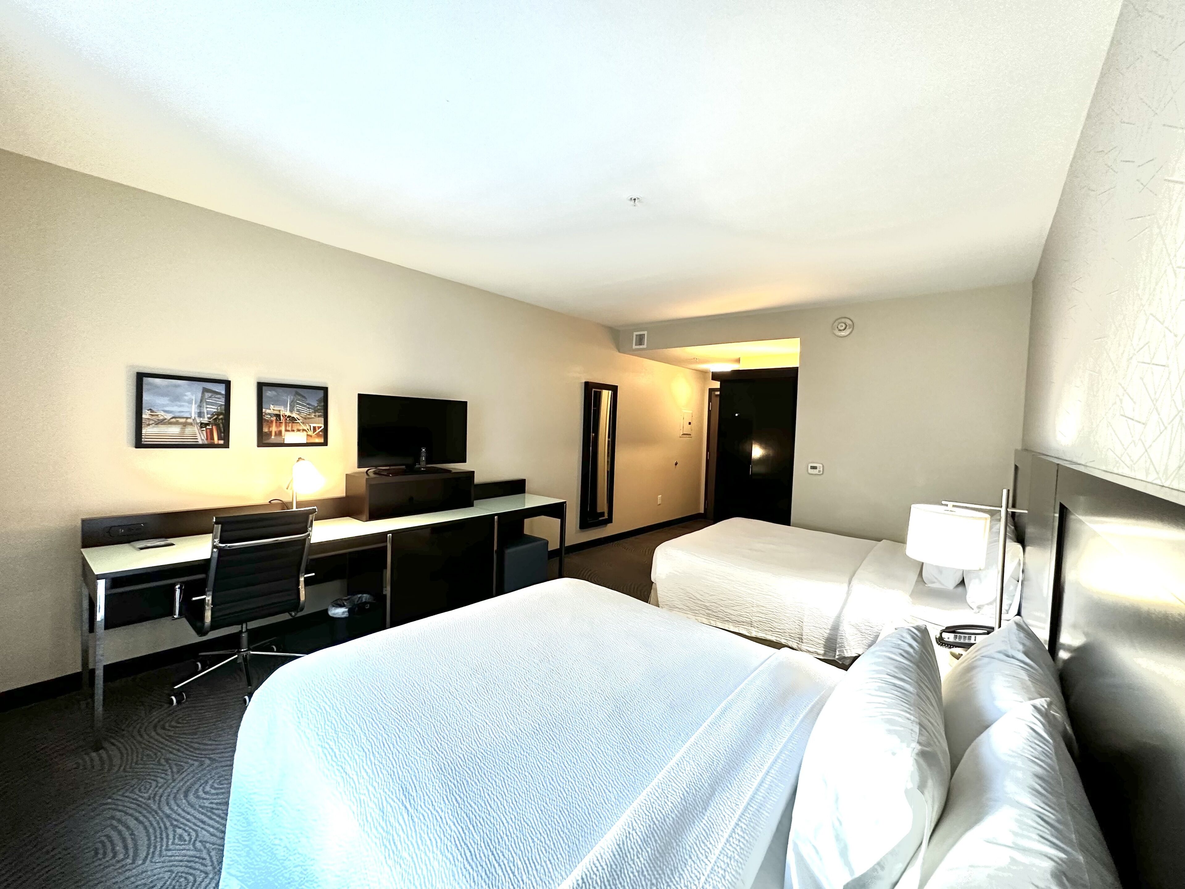 Habitación de hotel con cama, escritorio con silla, televisión y dos cuadros en la pared.
