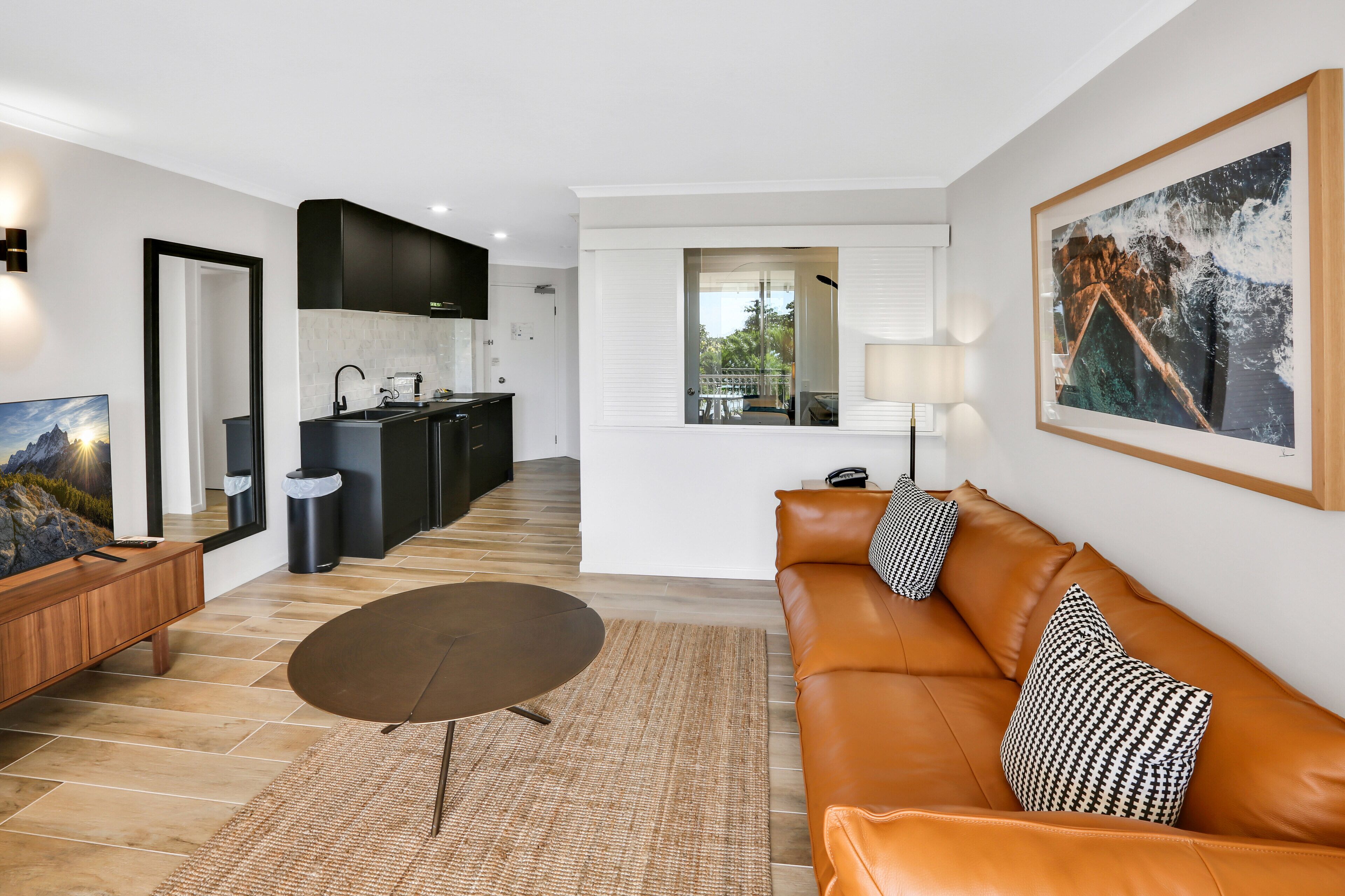 A modern living room with a brown leather sofa, a round coffee table, and a TV on a wooden stand.