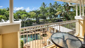A balcony with a view of a pool and palm trees, a table, and chairs. - On the Beach Holiday Apartments (Trinity Beach)