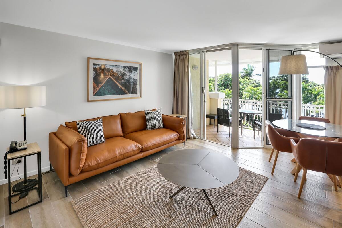 A modern living room with a brown leather sofa, a round coffee table, and a dining area with a table and chairs.