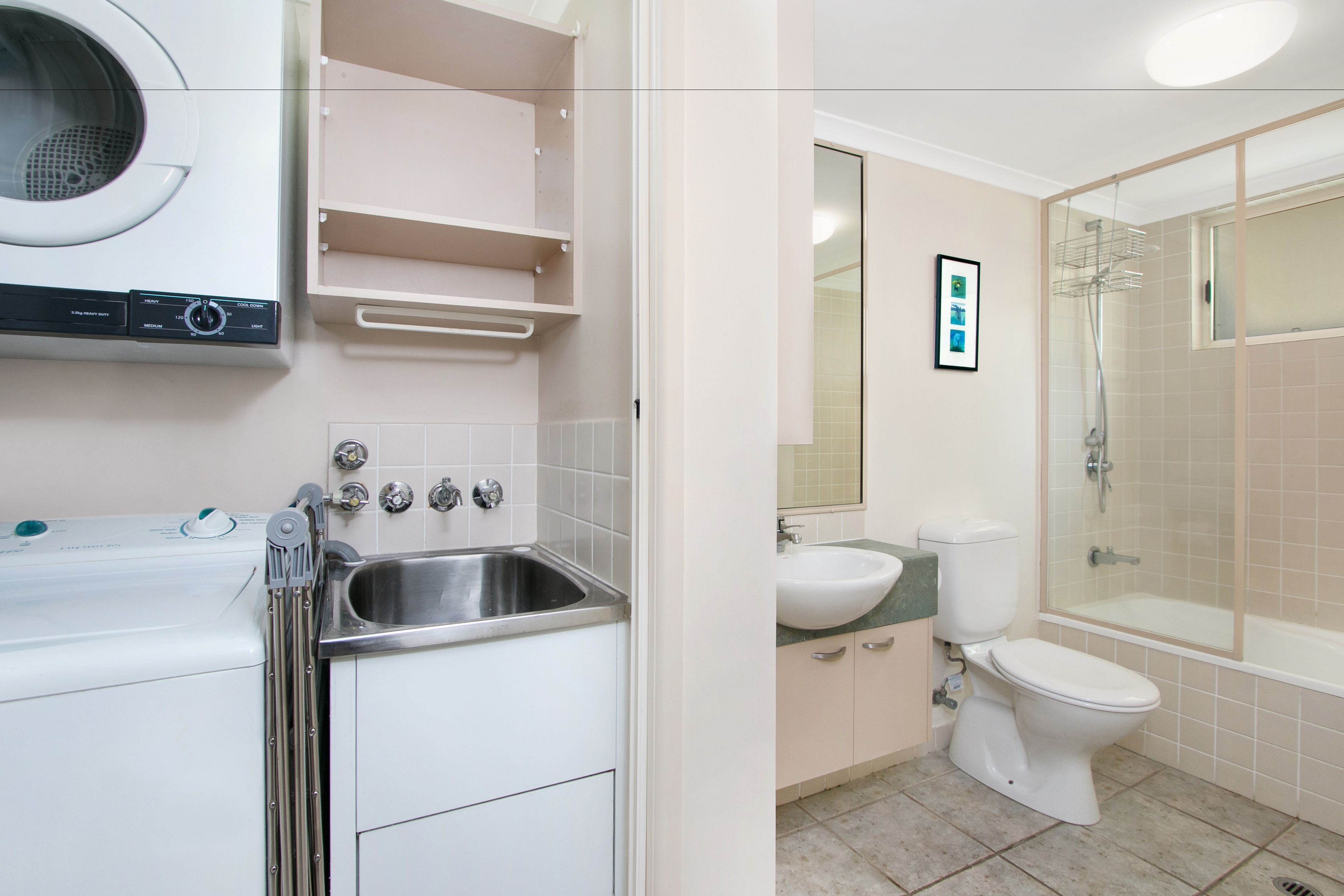 Une salle de bain moderne équipée d’un lave-linge intégré, d’un lavabo, de toilettes et d’une douche à parois de verre.