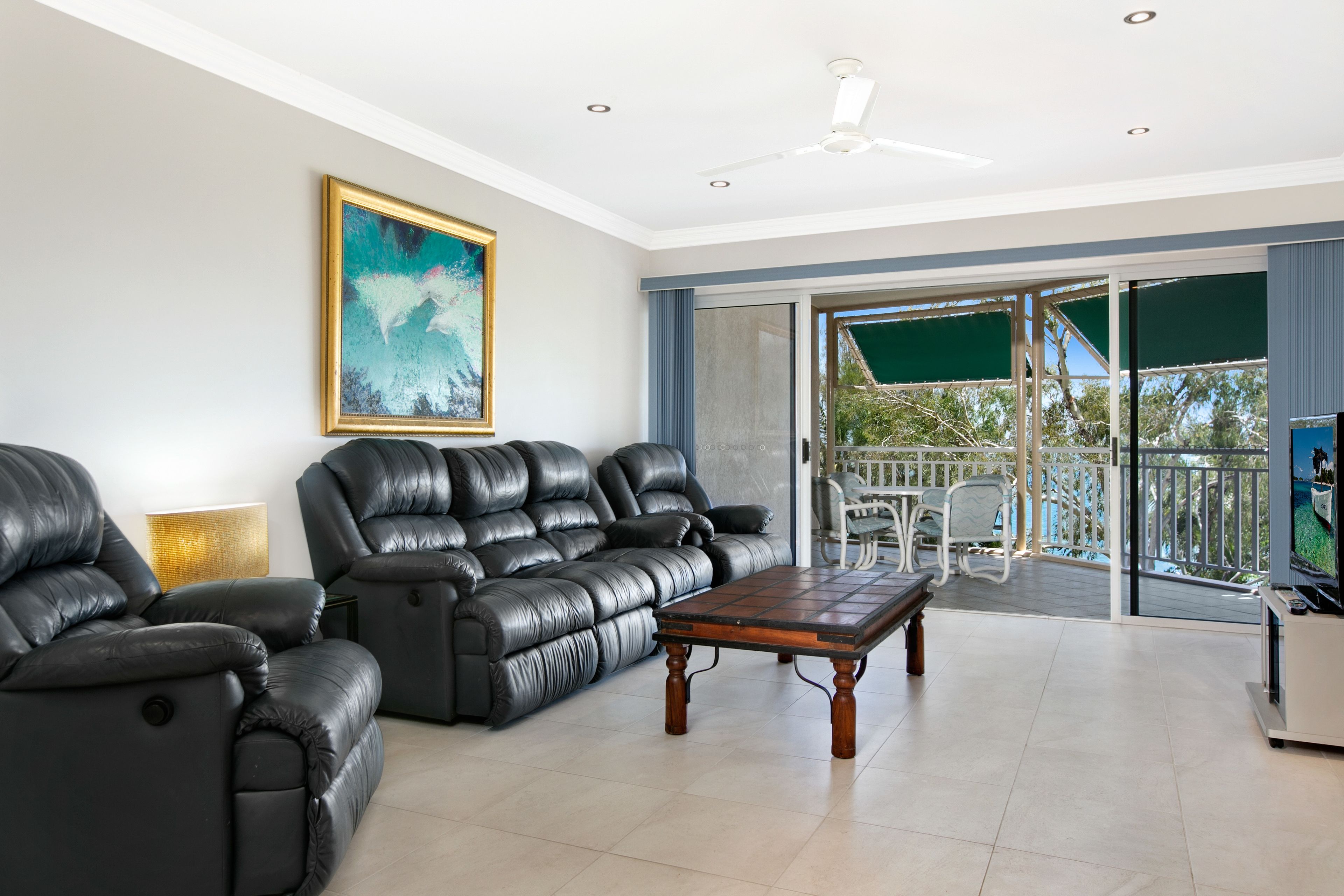 A living room with black leather sofas, a wooden coffee table, and a painting on the wall.