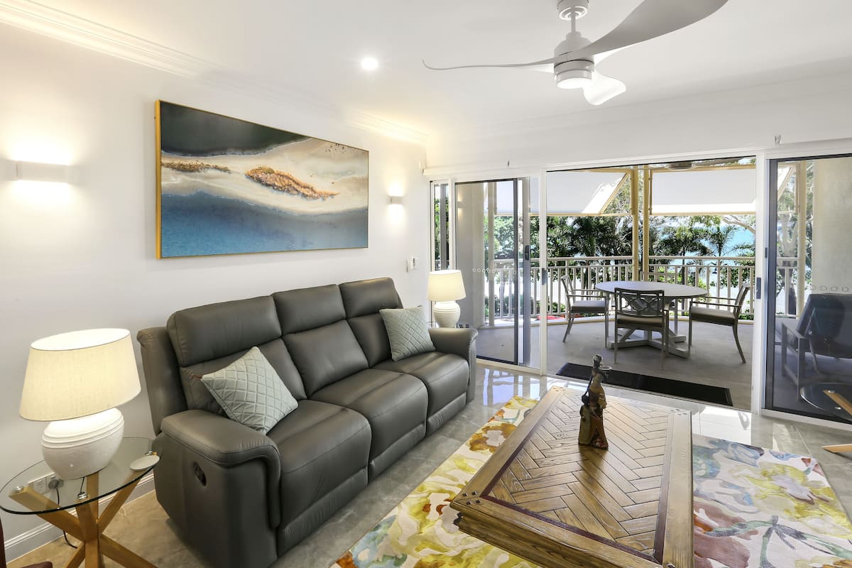 A modern living room with a leather sofa, a glass coffee table, and a painting on the wall.