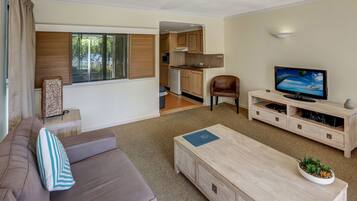 A modern living room with a sofa, a coffee table, a TV, and a kitchen in the background.