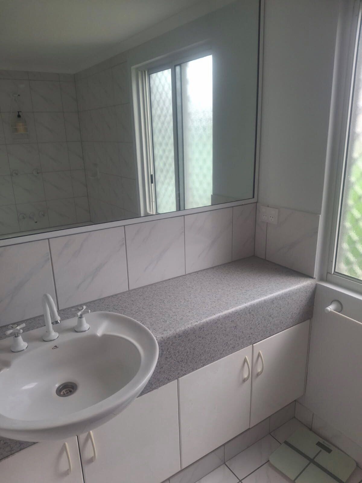 Une salle de bain avec un lavabo blanc, deux robinets, un miroir et une fenêtre en verre dépoli.
