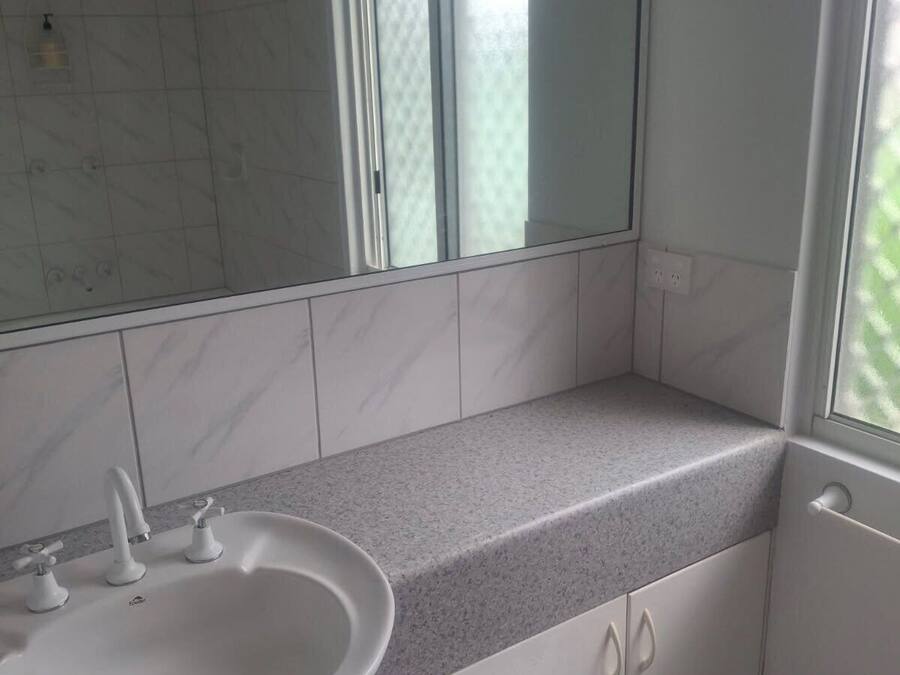 Een badkamer met een witte wastafel, twee kraanwerkstukken, een spiegel en een raam met geëtst glas.