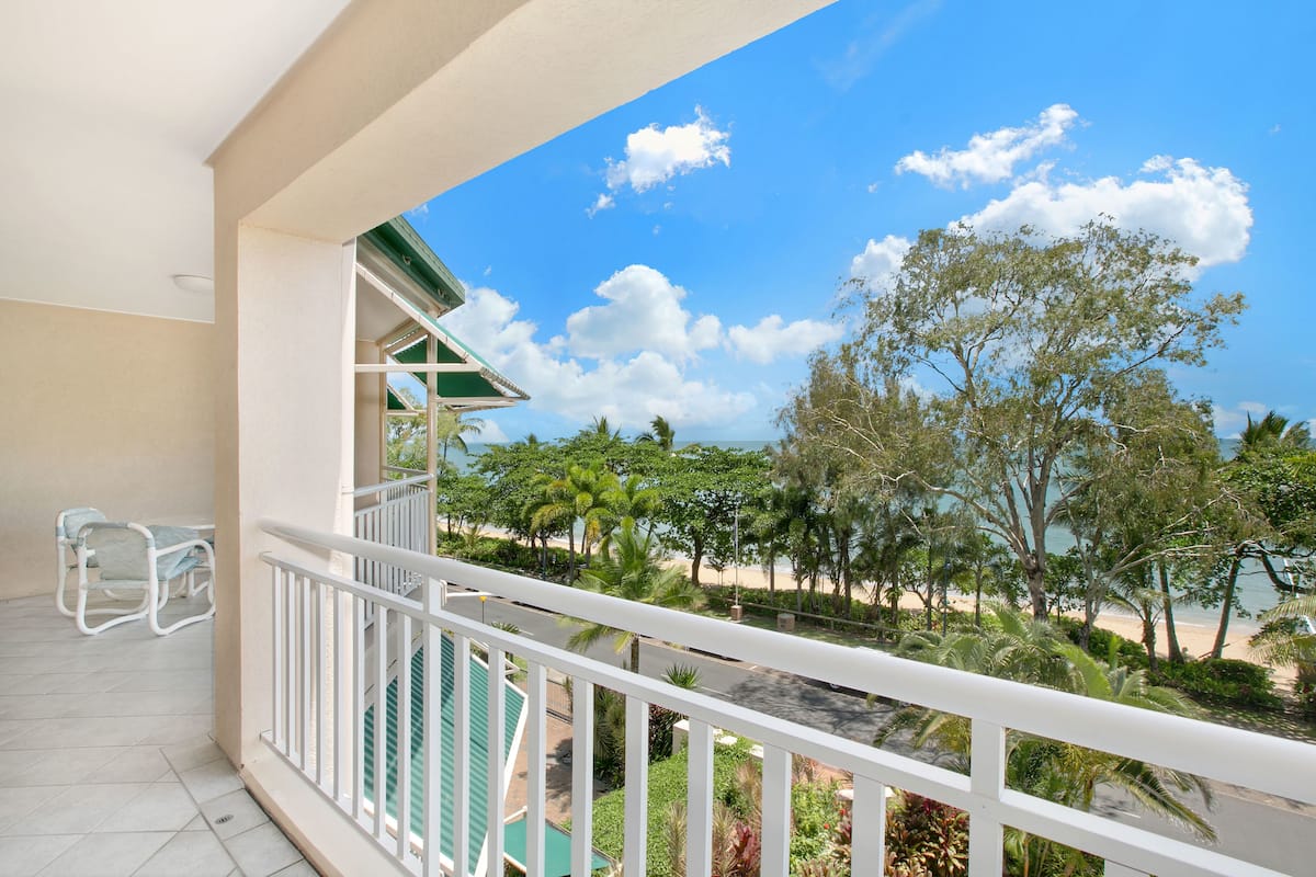 A balcony with a view of a beach, palm trees, and a clear sky.