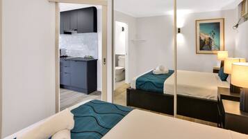 A hotel room with two beds, a small desk, a mirror, and a view of the kitchen and bathroom.