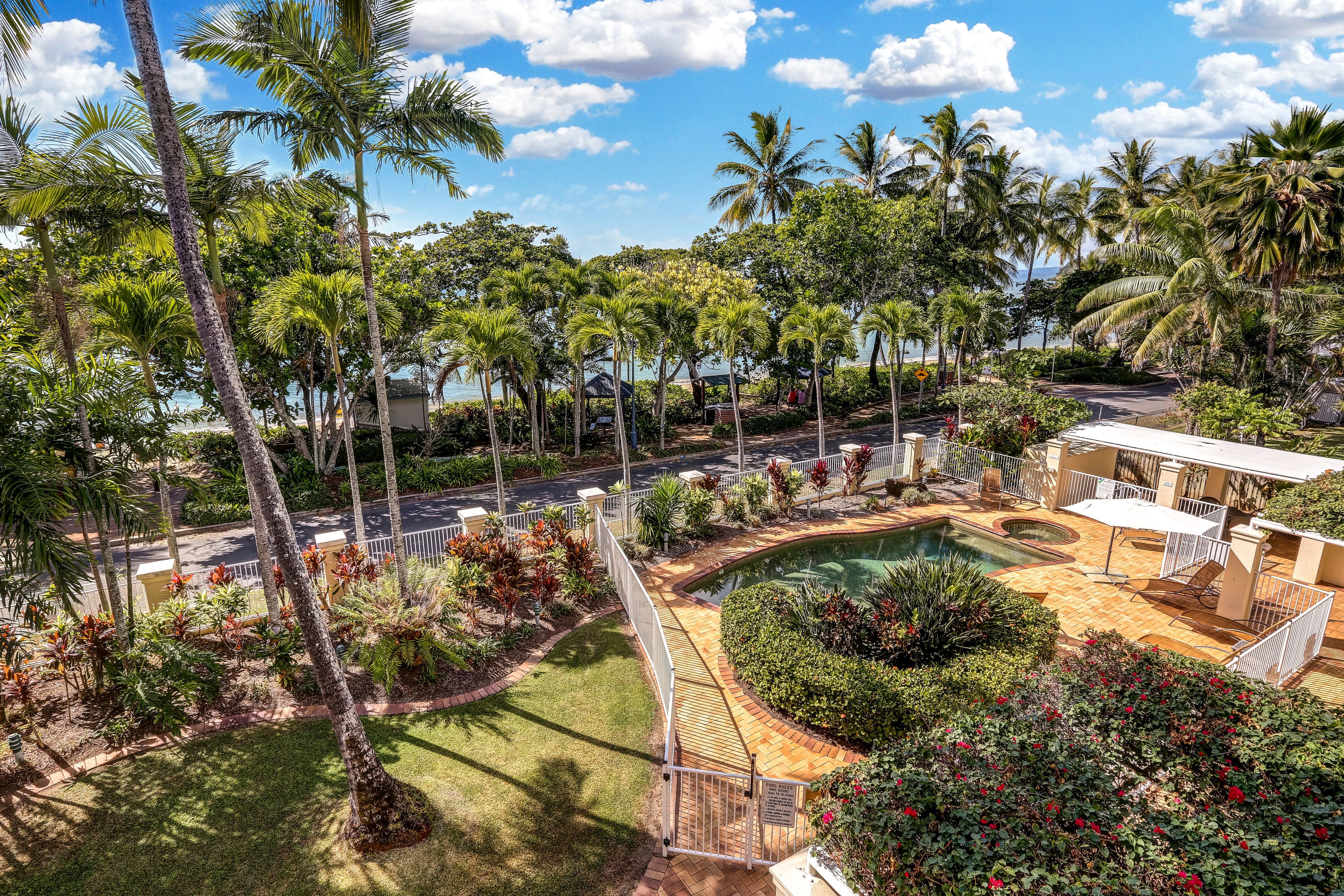 A pool area with palm trees, a patio, and a view of the road.