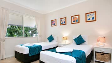 Habitación de hotel con dos camas, una ventana con cortinas, una mesita de noche con lámpara y decoración en la pared.