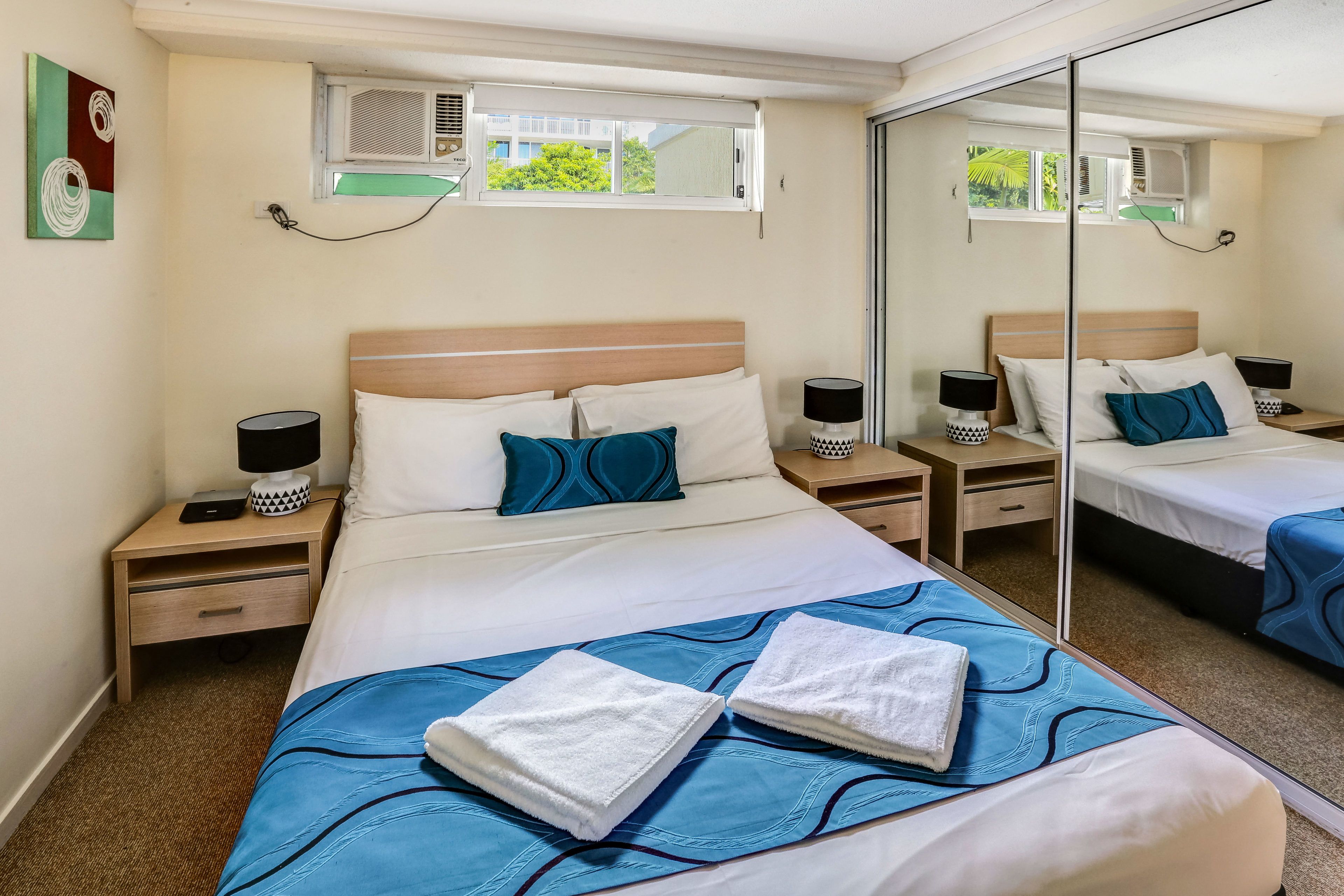 A hotel room with a large bed, two bedside tables with lamps, a mirror, and an air conditioning unit.