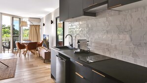 A modern kitchen with a black countertop, white marble backsplash, and a dining area with wooden chairs and a table. - On the Beach Holiday Apartments (Trinity Beach)
