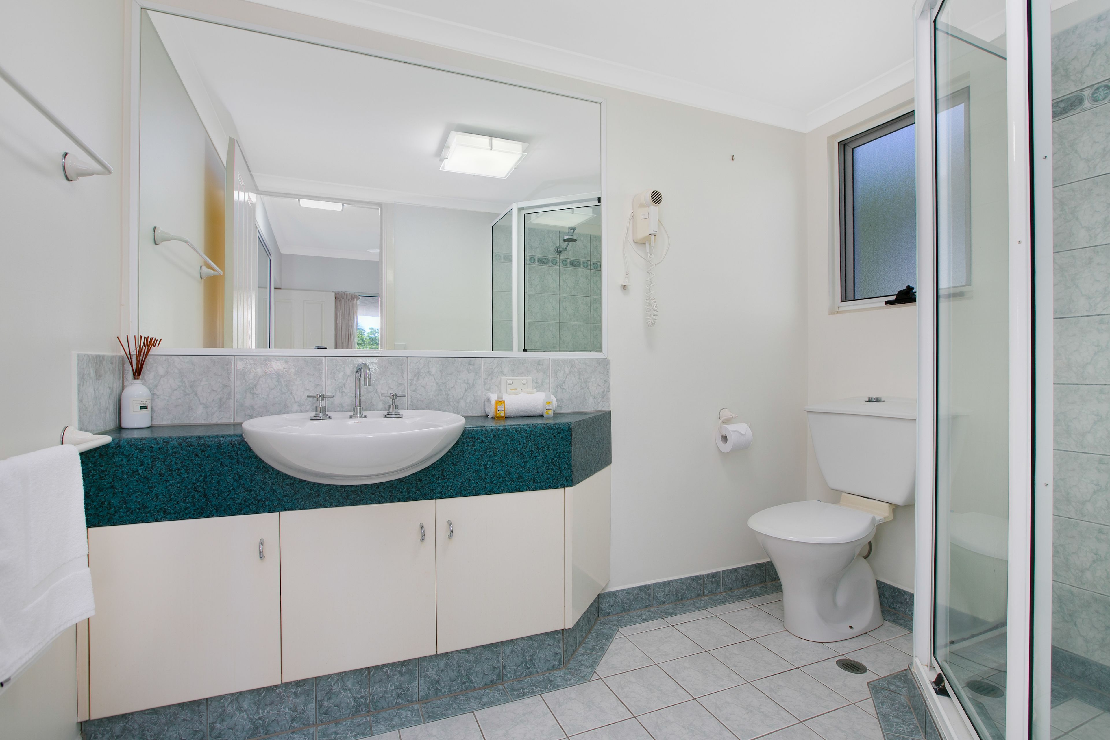 A modern bathroom with a white sink, teal countertop, and a large mirror.