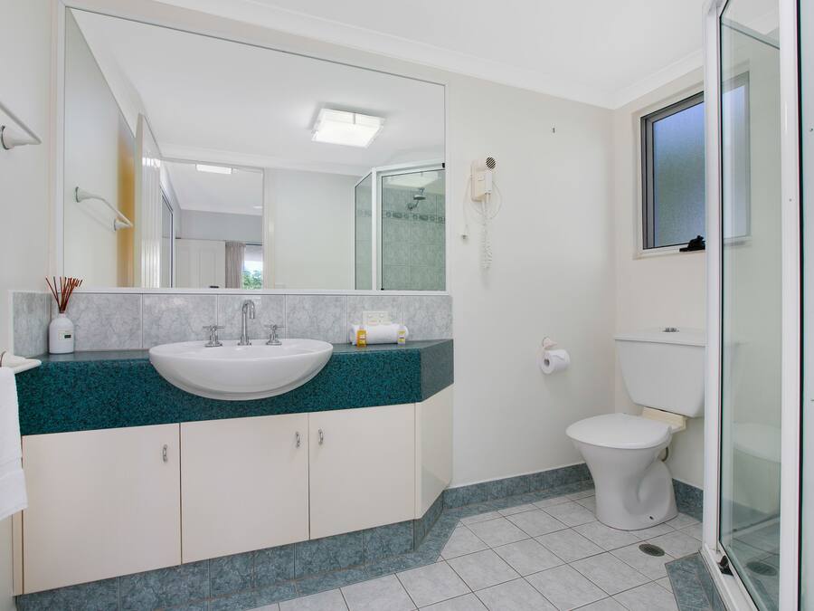 A modern bathroom with a white sink, teal countertop, and a large mirror.
