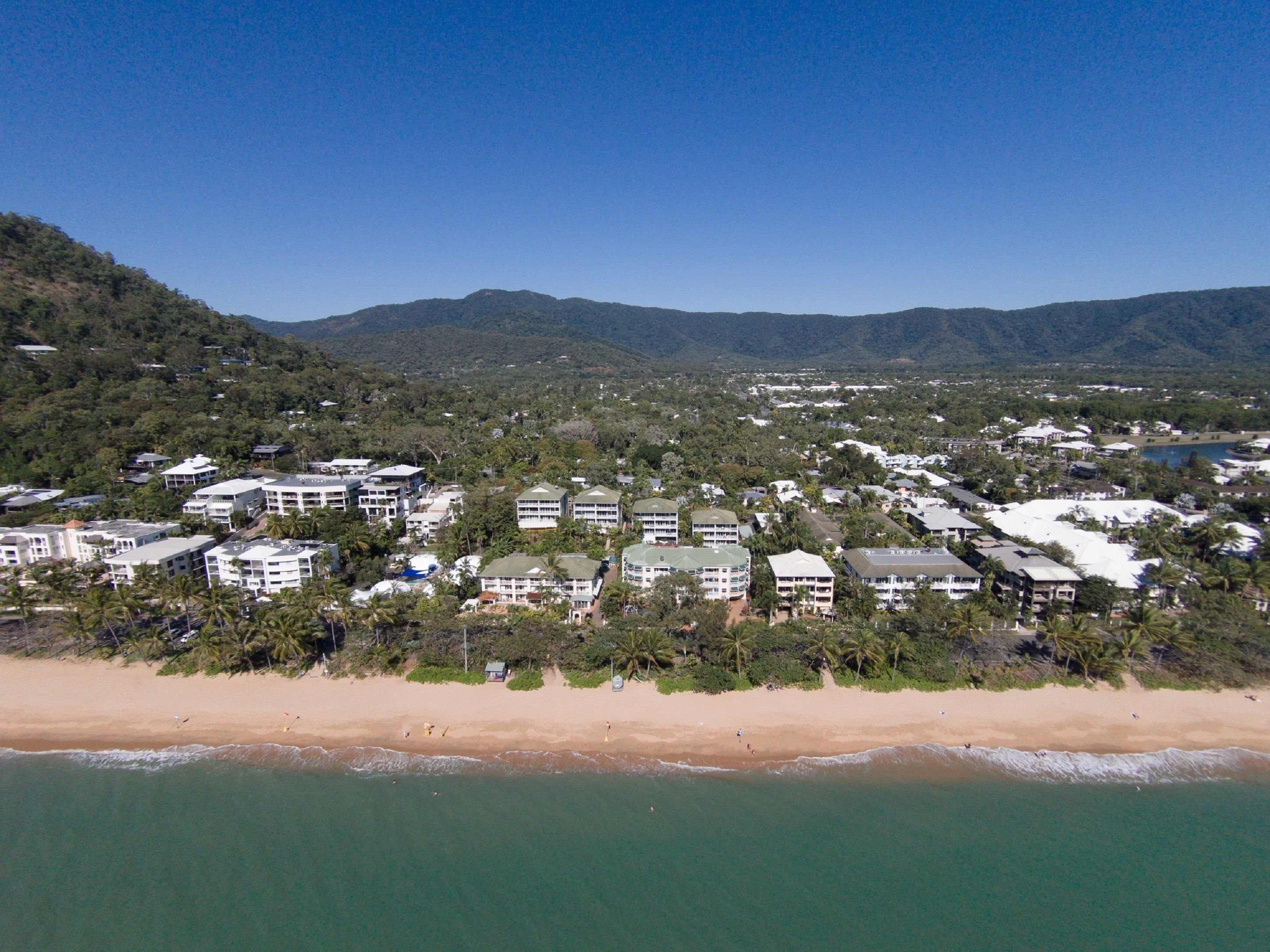 Eine Luftaufnahme eines Küstenresorts mit mehreren Gebäuden, einem Sandstrand und einer Hügelkulisse.