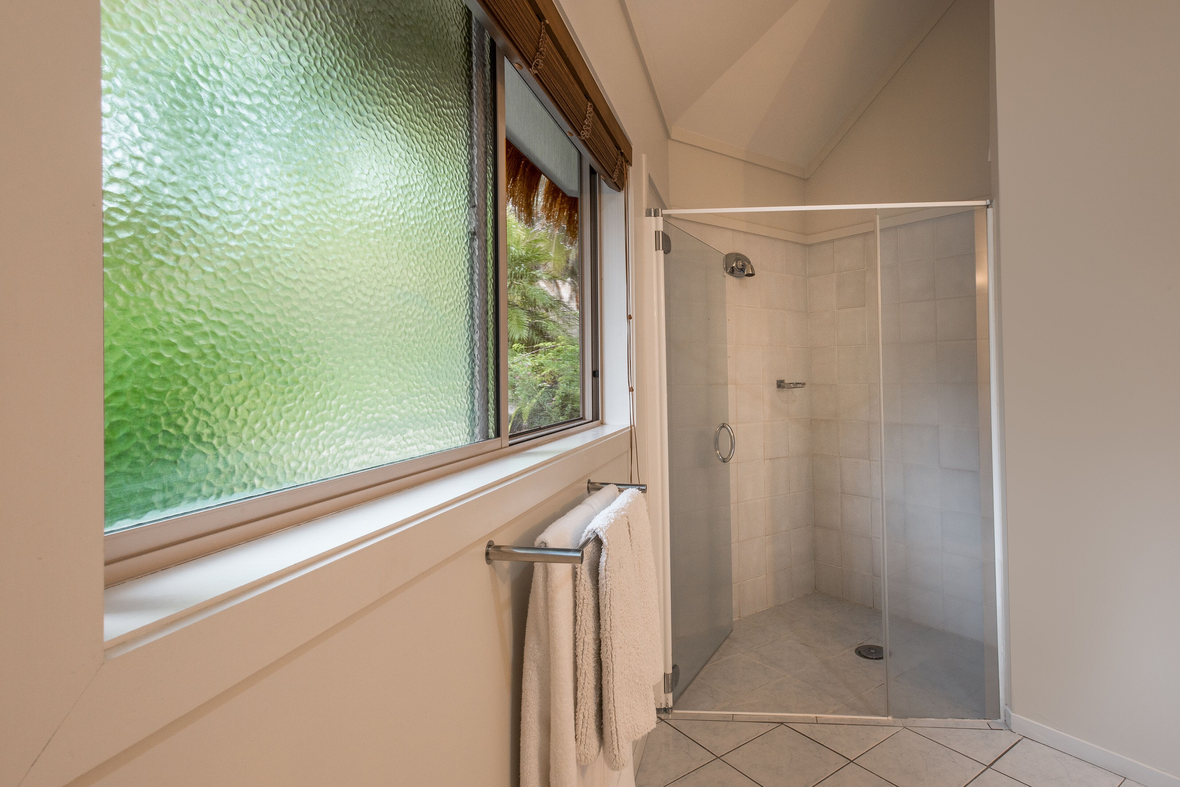 Un baño con cabina de ducha de vidrio, una ventana con cristal texturizado y un perchero para toallas.