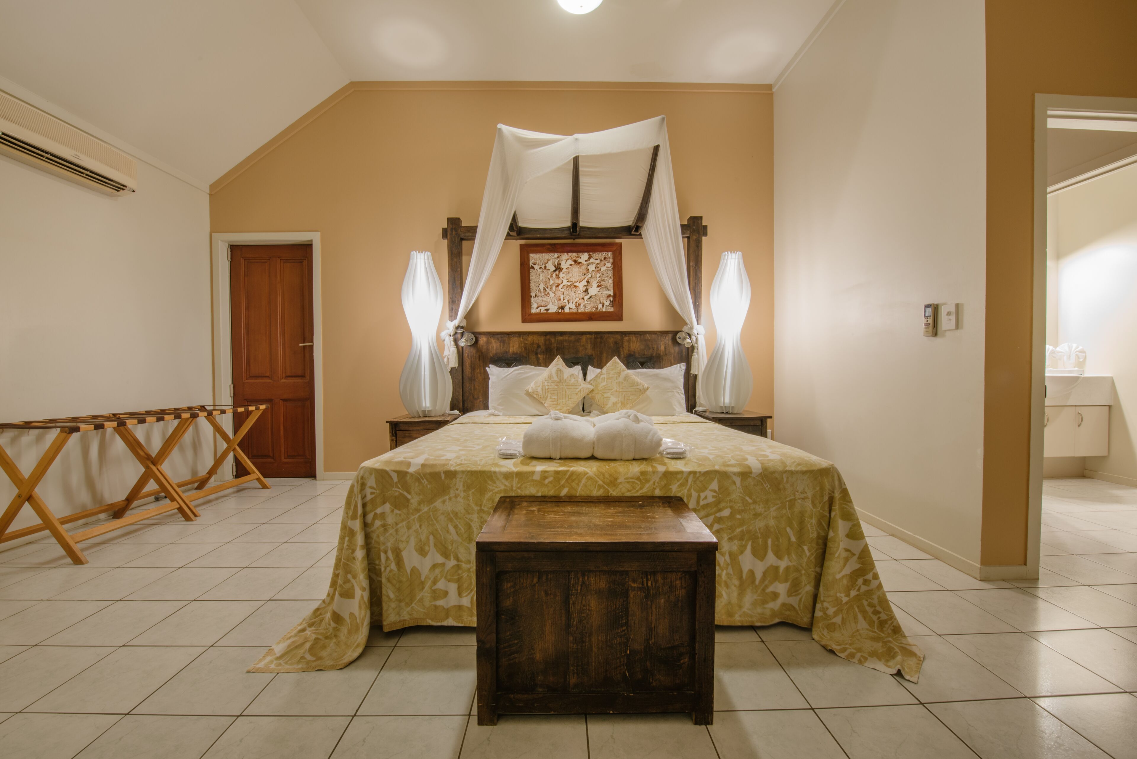 A bedroom with a bed, a wooden bench, a wooden headboard, a nightstand, a bedside table, and a door.