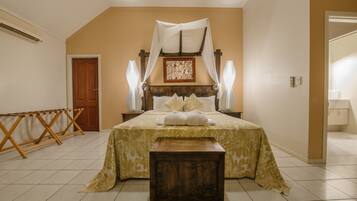 A bedroom with a bed, a wooden bench, a wooden headboard, a nightstand, a bedside table, and a door.